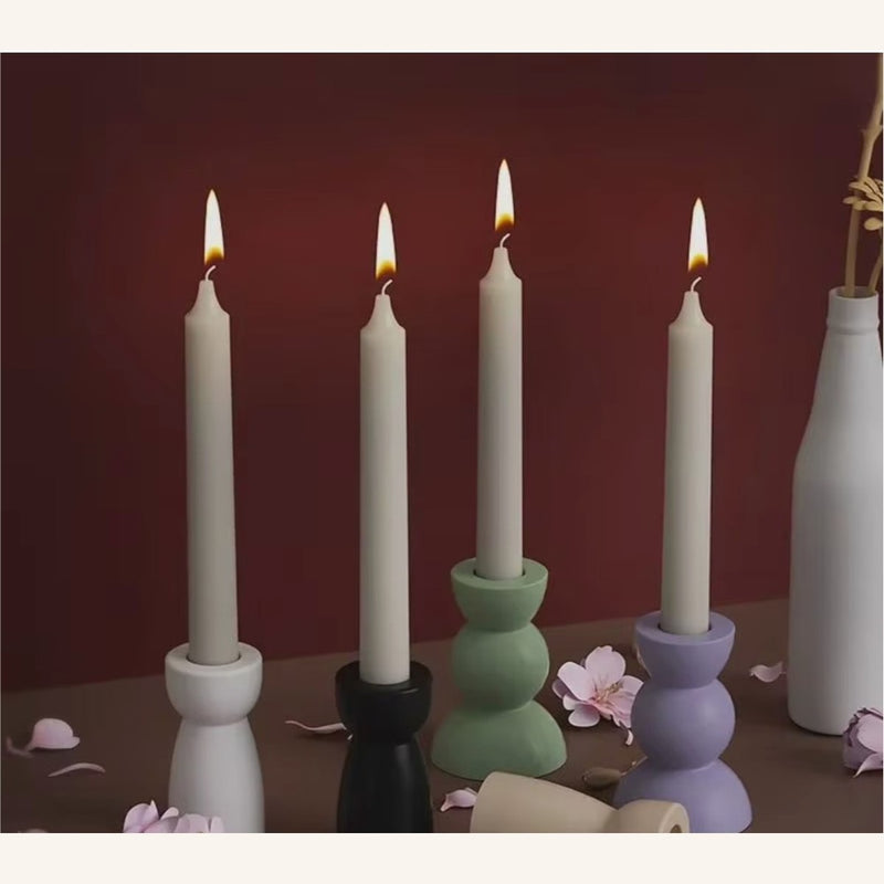 Four geometric candle holders in pastel and monochrome colors with lit candles